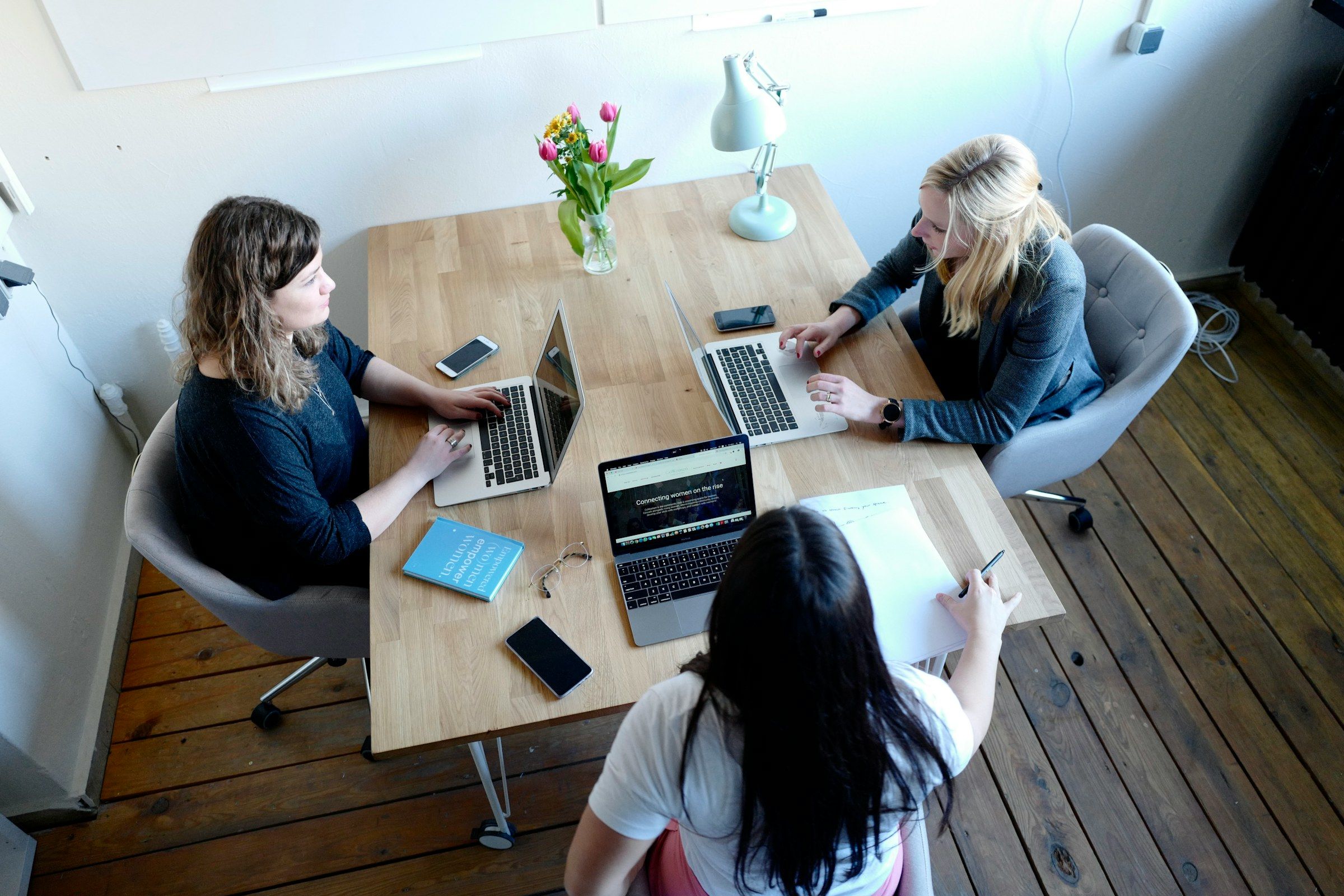 Seen from above: three colleagues work together around a table, laptops open.