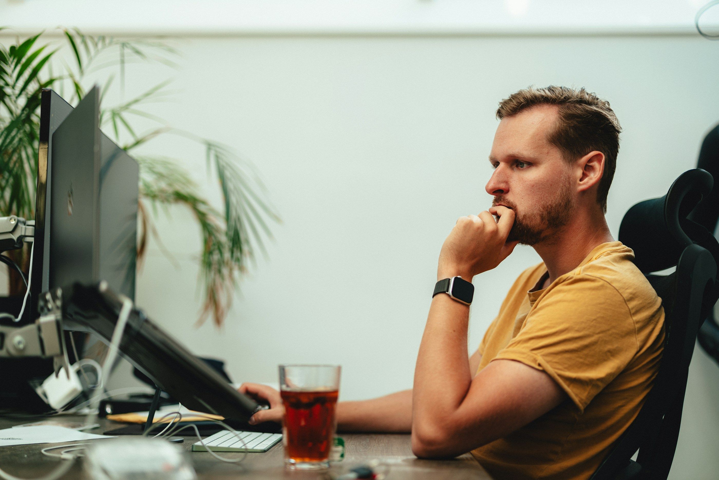 In an office, an employee sits at a desk, chin in hand, gazing at the screen, deep in thought.