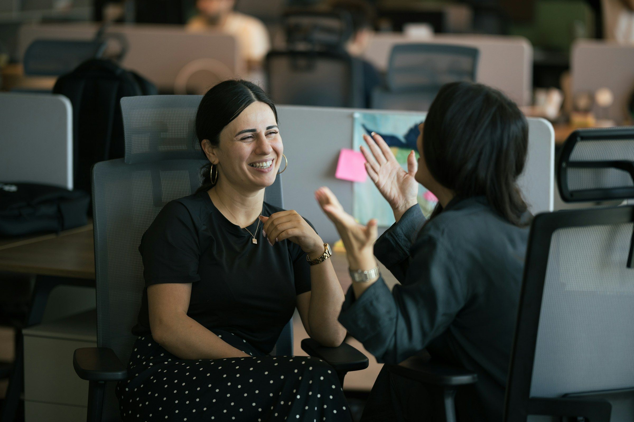 Two colleagues laugh together in an open-plan office.