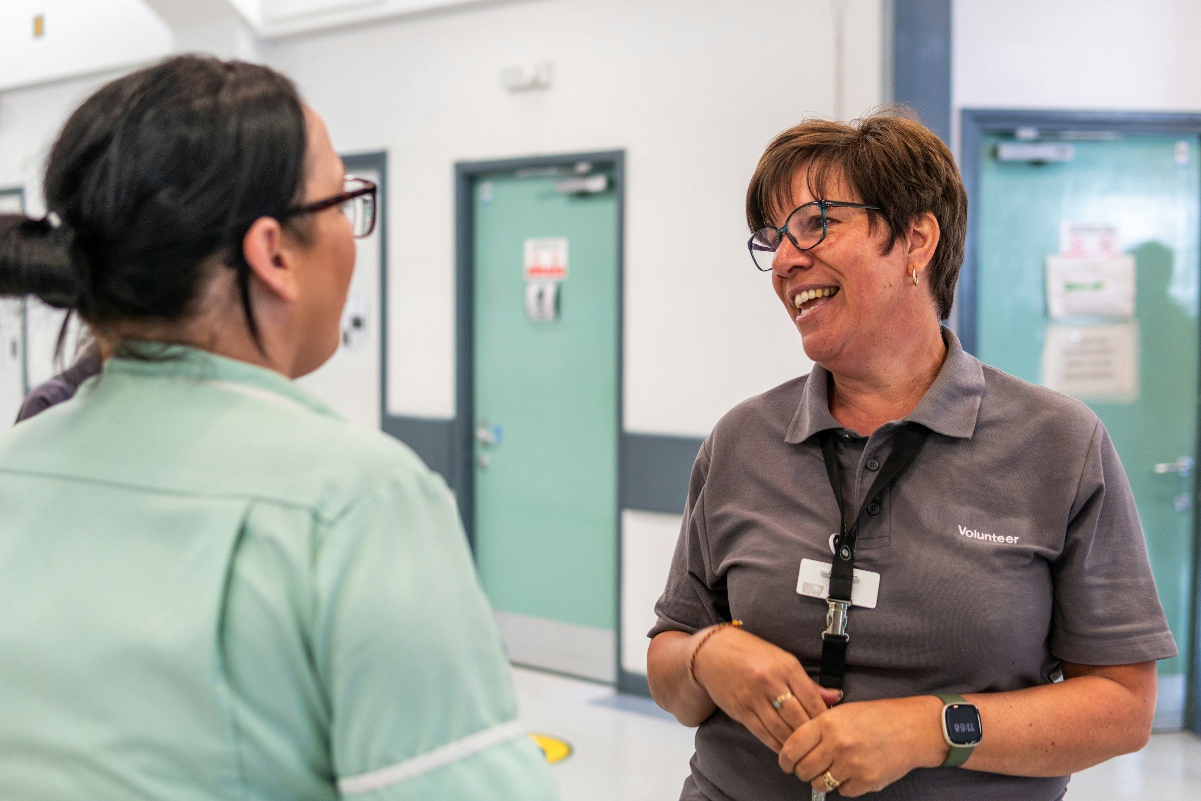 Two women chat and smile in a hospital corridor.